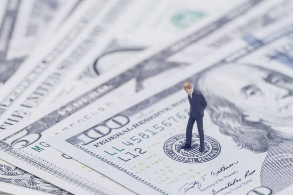 Small figure of a man in a suit standing on a stack of U.S. dollar bills