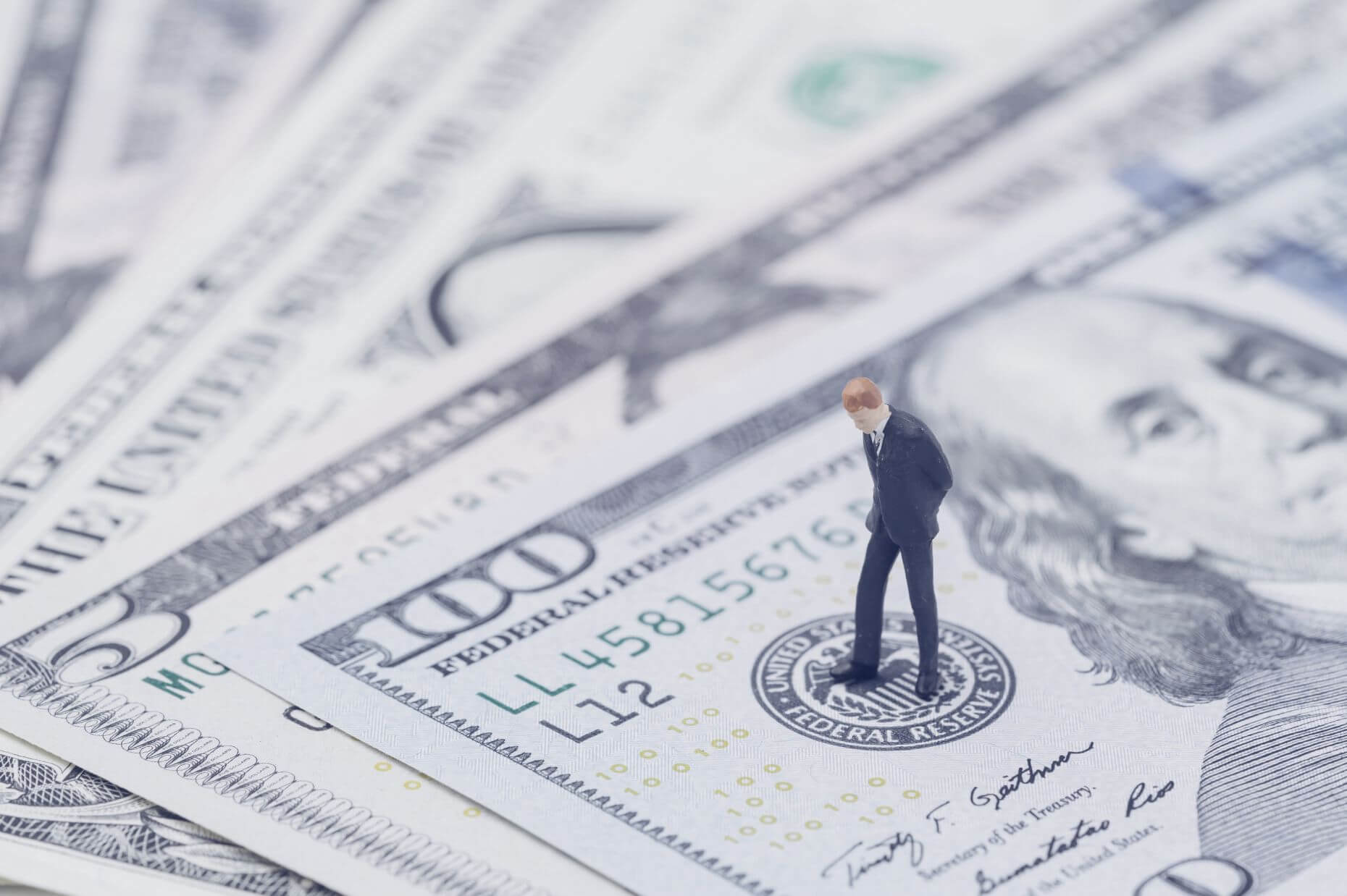 Small figure of a man in a suit standing on a stack of U.S. dollar bills