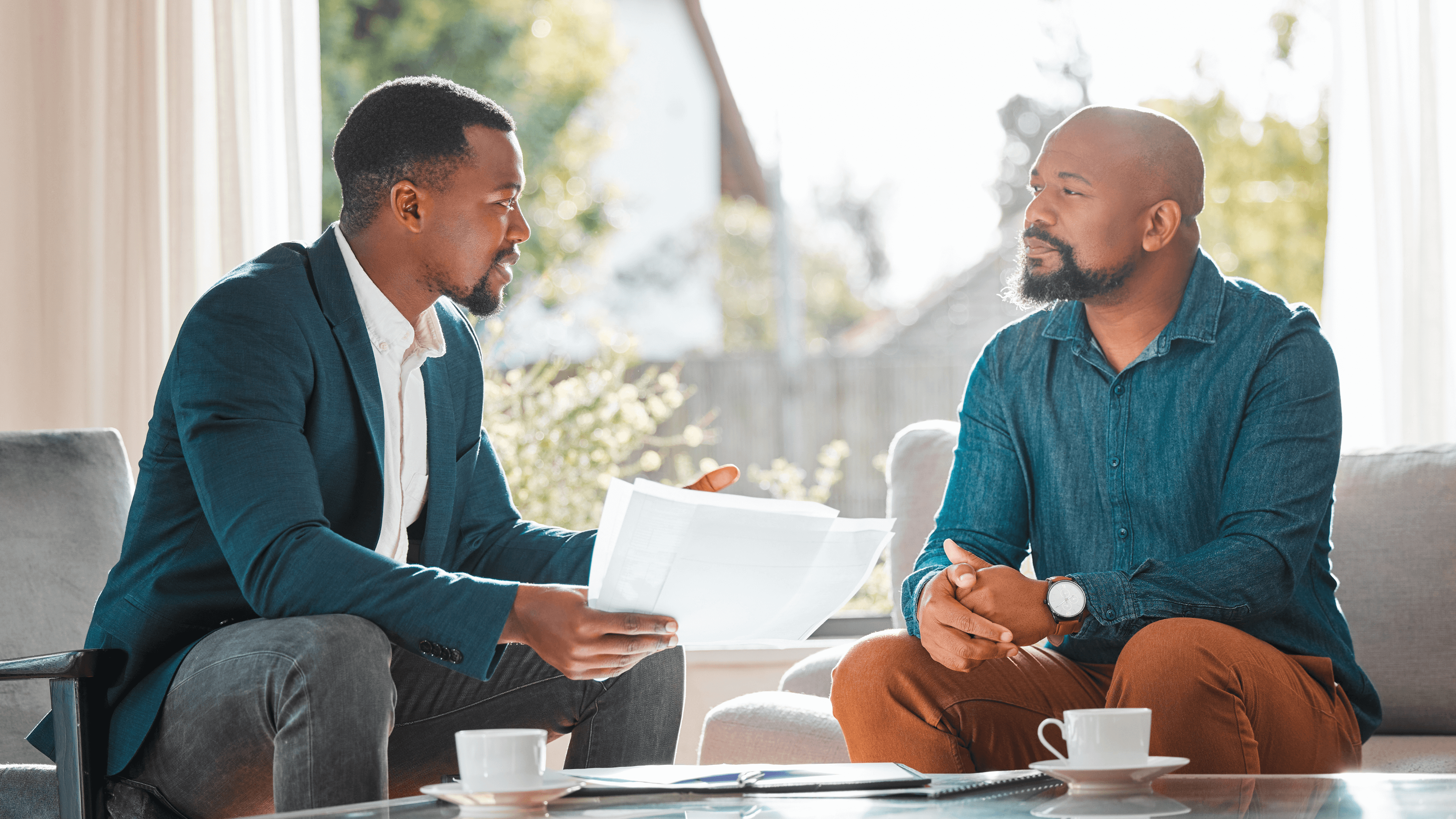 Two gentlemen conversing together sitting with 2 tea cups on coffee table
